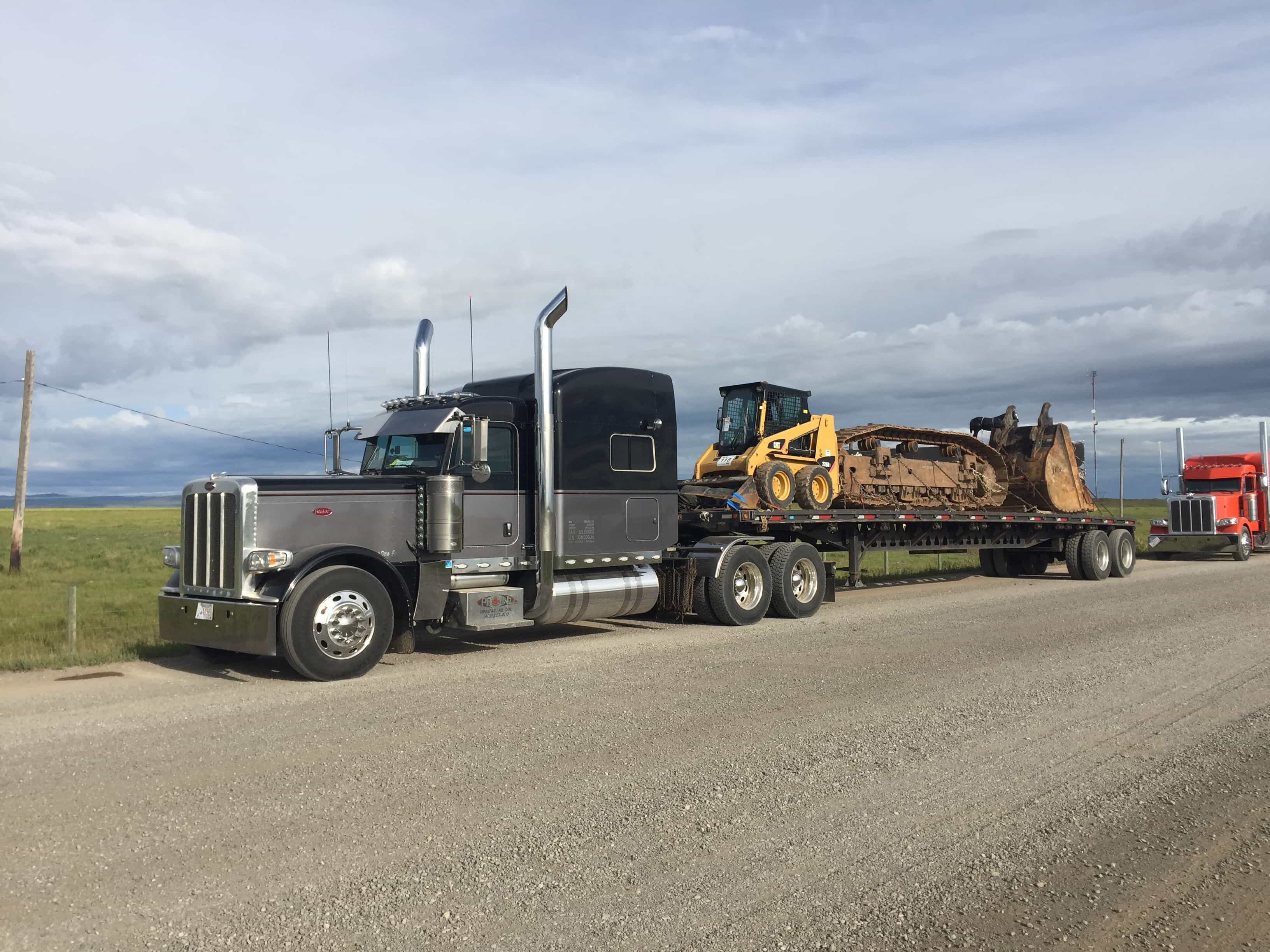 A truck using a flat bed to haul a small bulldozer and parts of another construction vehicle